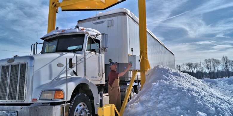 a semi truck driving under a scraper system in winter